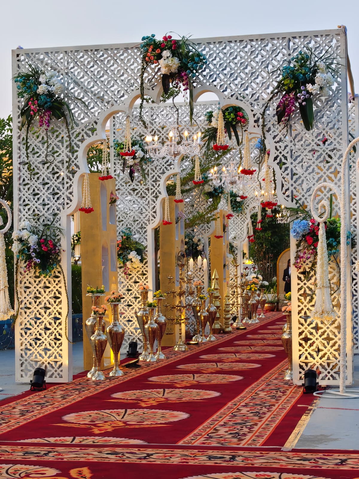 Floral jaali entry walkway with chandeliers and brass urns
