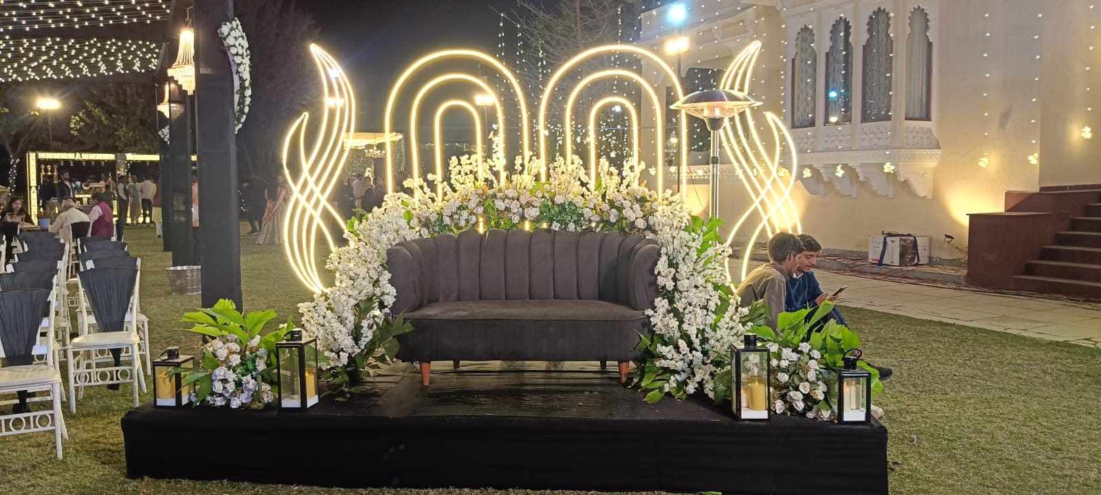 Illuminated reception stage with white florals and neon arches